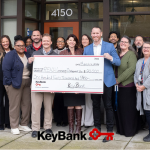 REACH and KeyBank staff gather around a large check
